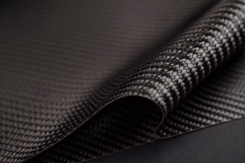 Aufgerollte Carbonmatte mit sichtbarer Köperbindung auf dunklem Untergrund