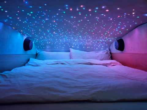Doppelbett auf der Schlafebene des VANYX unter einem beleuchteten Sternenhimmel in der Dachschale, seitlich eingelassene Lautsprecher