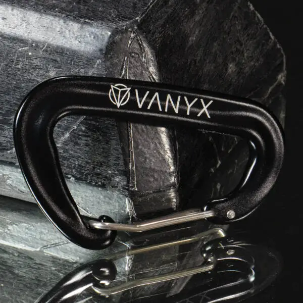 Schwarzer Vanyx Karabiner aus Aluminium mit Logo – liegend auf Stein