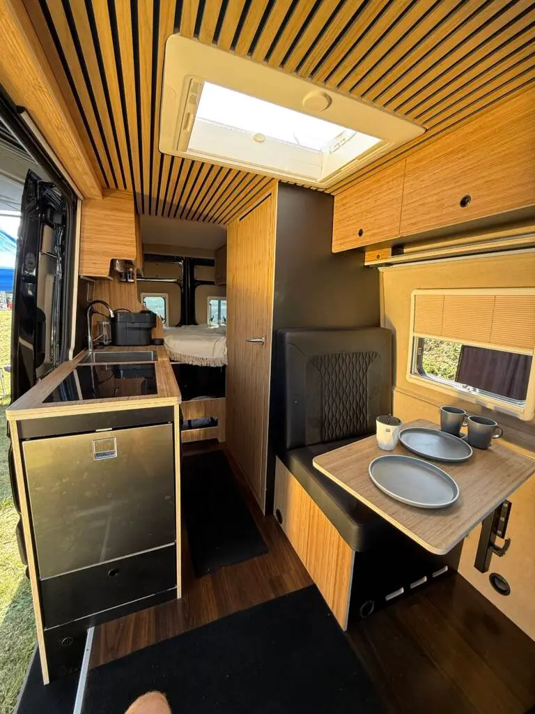 Innenansicht eines MAN TGE 180 4x4 Campervans mit Küche, Sitzgruppe und Schlafbereich