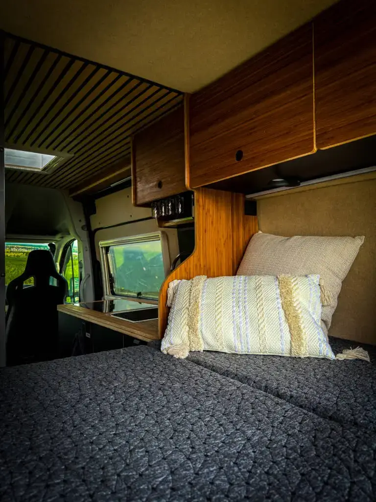 Gemütlicher Schlafbereich mit Holzelementen, Kissen und Dachverkleidung im 4x4 Campervan