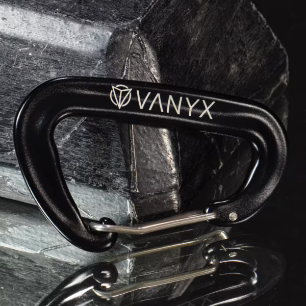 Schwarzer Vanyx Karabiner aus Aluminium mit Logo – liegend auf Stein
